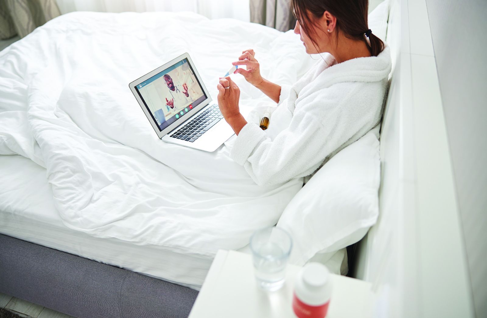 Hotel guest consulting a doctor from her bed via laptop